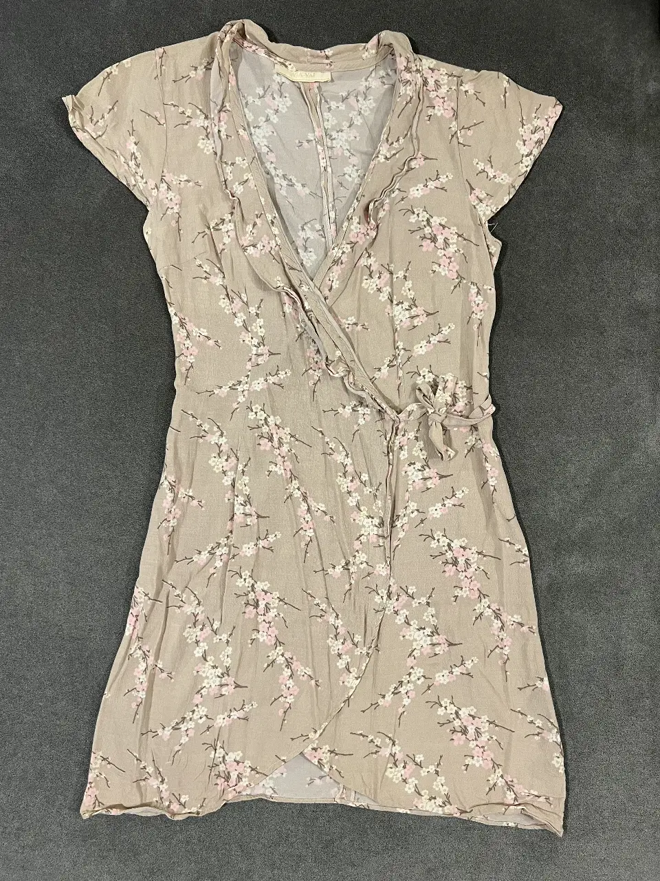 Vestido mini de mujer con estampado floral en tonos crudo y rosa. Diseño envolvente con detalle de lazo en la cintura y mangas cortas. Ideal para un look fresco y femenino.