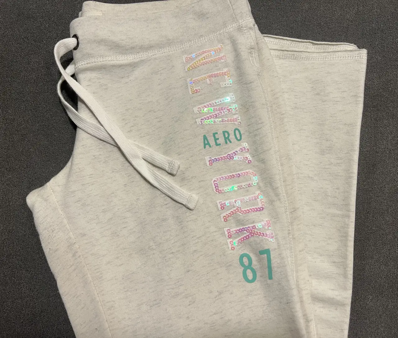 Pantalón de jogging Aeropostale para mujer, color blanco jaspeado tipo cremita con detalles en lentejuelas. Talle M. Es apretado arriba y suelto a partir de las rodillas 
