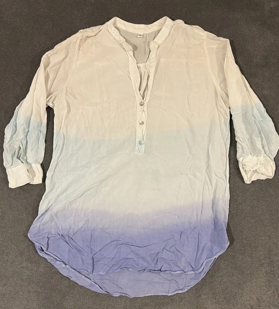 Blusa de mujer con diseño degradado en tonos blanco y azul. Cuello en V, manga larga con puños y botones. Ideal para un look casual y fresco.