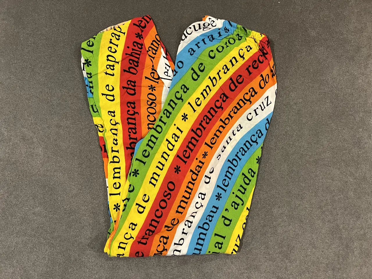 Pantalón suelto con estampado de arcoíris y frases en portugués. Ideal para un look bohemio y llamativo.