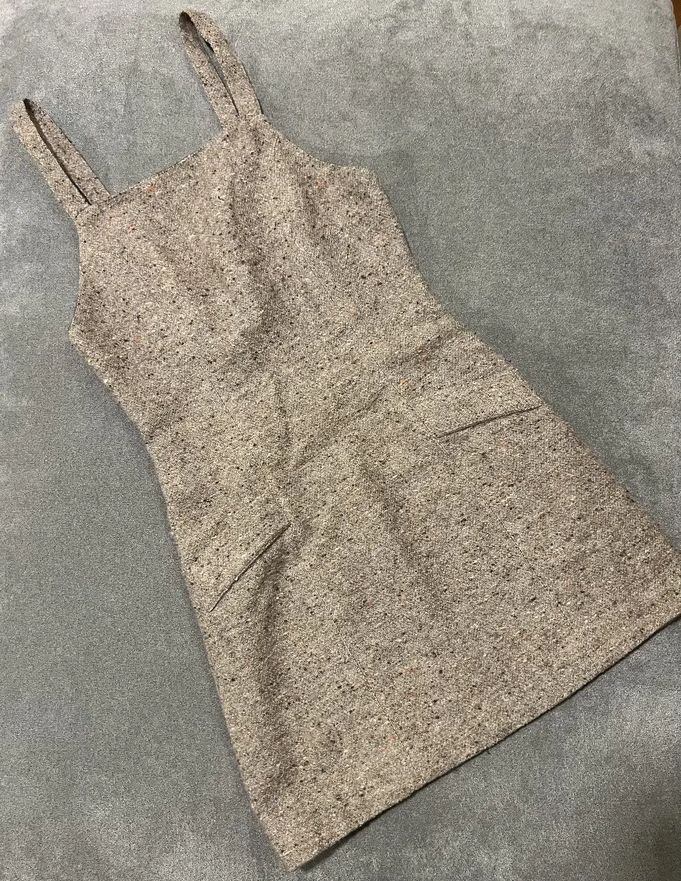 Vestido mini de tela tweed con tirantes finos y bolsillos delanteros. Diseño vintage con cierre y botones en la espalda. Ideal para un look elegante y retro.