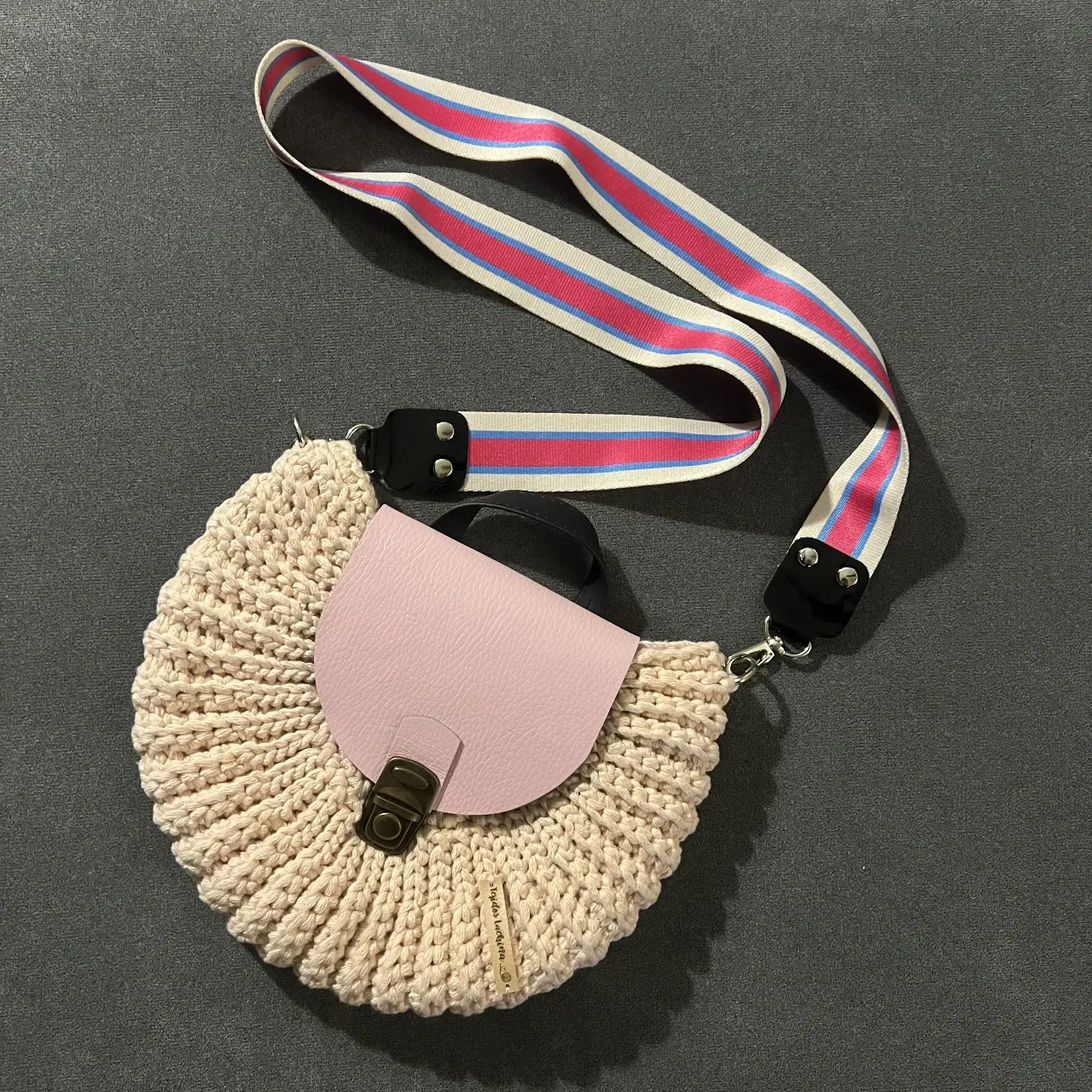 Cartera bandolera artesanal de crochet en color rosa clarito con solapa de cuero rosa. hecha a mano, tejida. Detalles de cierre metálico y correa ajustable con diseño a rayas. Ideal para un look casual y bohemio. Nueva! Sin uso, viene con su bolsita