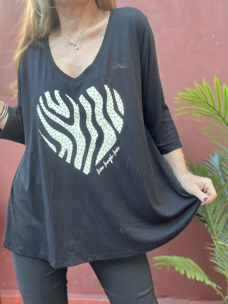 Remera negra con escote en V y manga 3/4. Estampado de corazón con diseño de cebra en blanco. La frase 'live laugh love' está escrita en la parte inferior del corazón. Ideal para un look casual y cómodo.