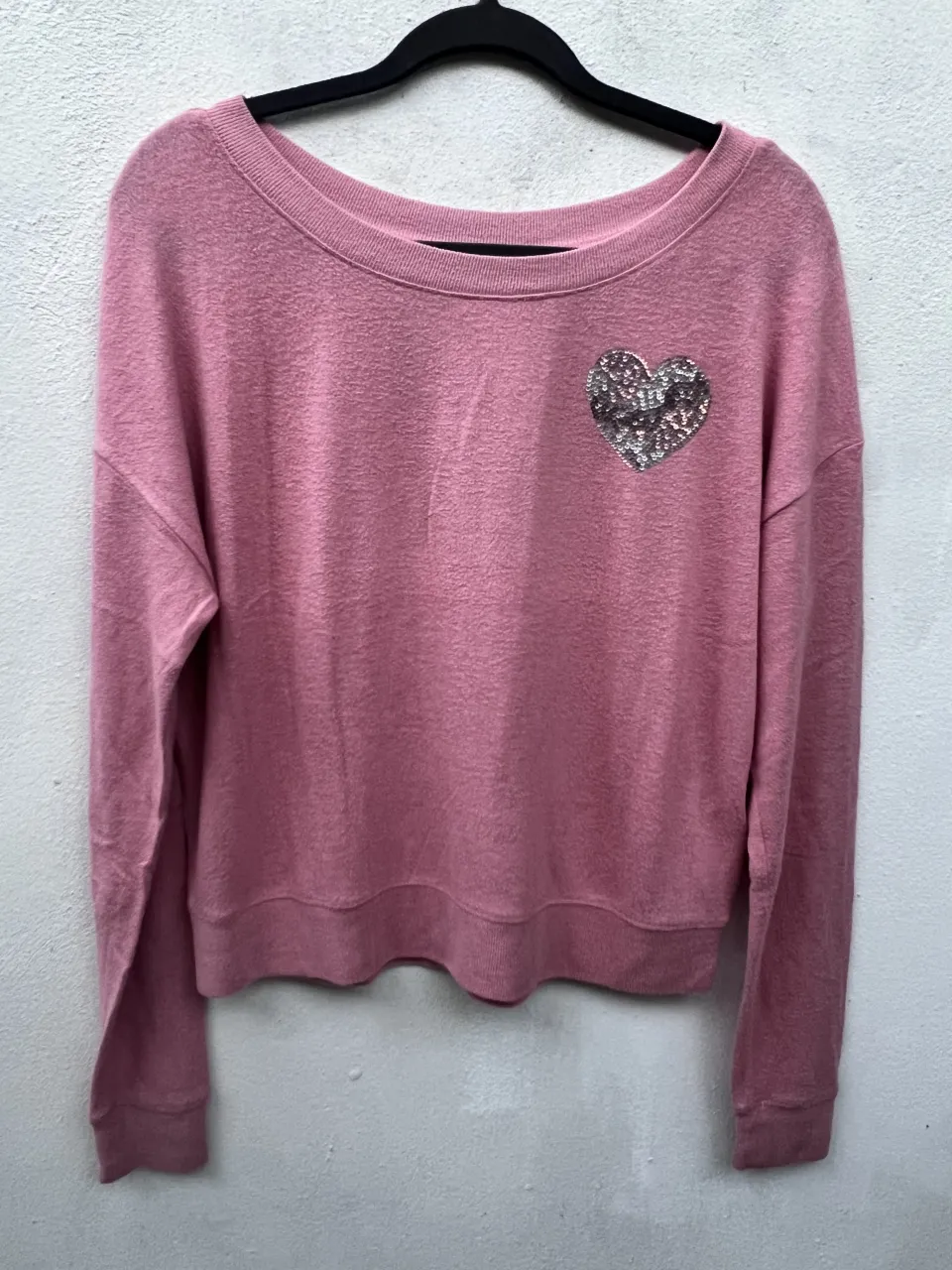 Sweater rosa con cuello redondo y manga larga. Posee un aplique de corazón con brillos en el frente.