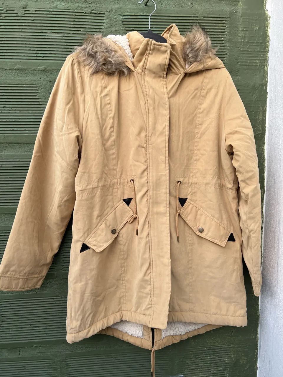 Campera color tiza con capucha forrada en corderito. Tiene bolsillos frontales con solapa y cordón ajustable en la cintura.