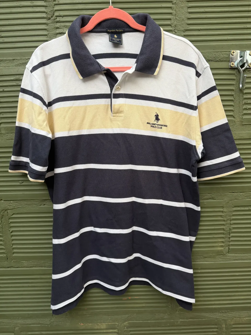 Remera polo a rayas horizontales en blanco, amarillo y azul marino. Cuello y puños en azul marino. Logo bordado en el pecho.