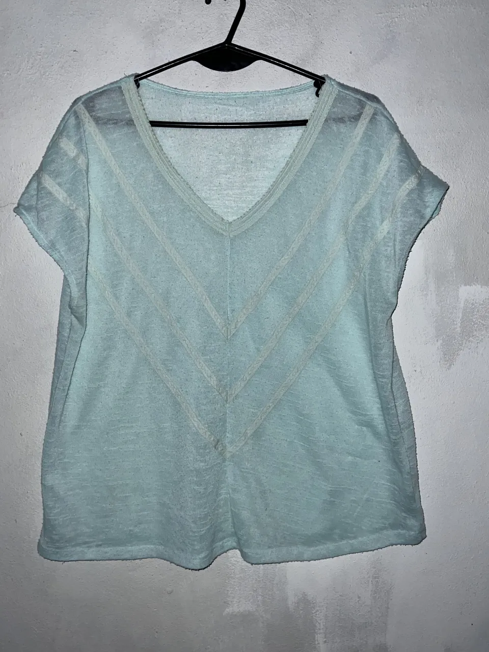 Remera de algodón color verde agua con cuello en V y detalles de puntilla en el frente. Posee mangas cortas.