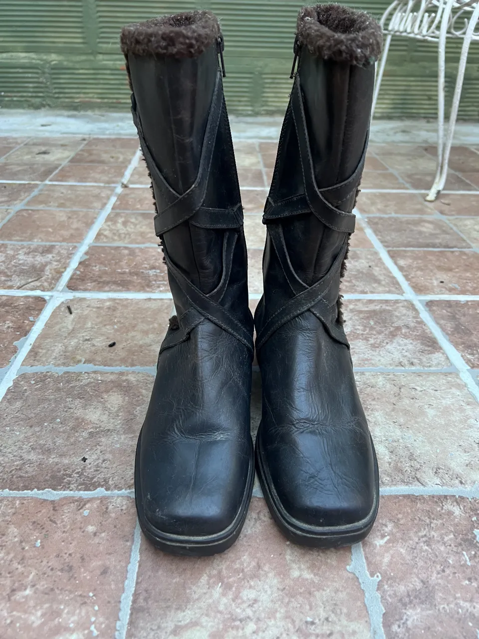 Botas de cuero marrones con detalles de tiras cruzadas y forro de peluche en la parte superior. Cierre lateral.