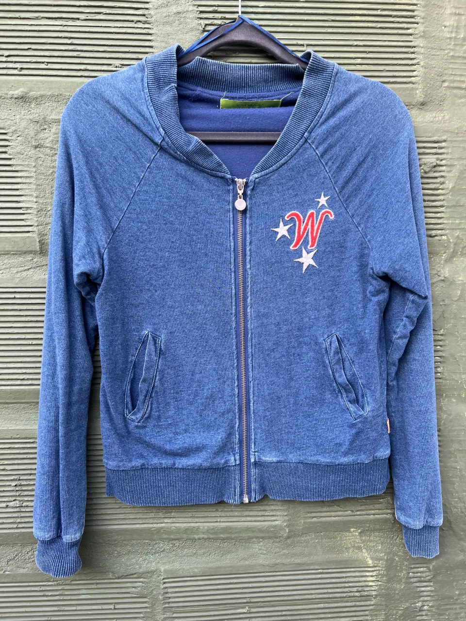 Campera bomber azul con cierre al frente y estampa de tigre y estrellas en la espalda. Tiene un logo bordado en el frente con la letra 'W' y estrellas.