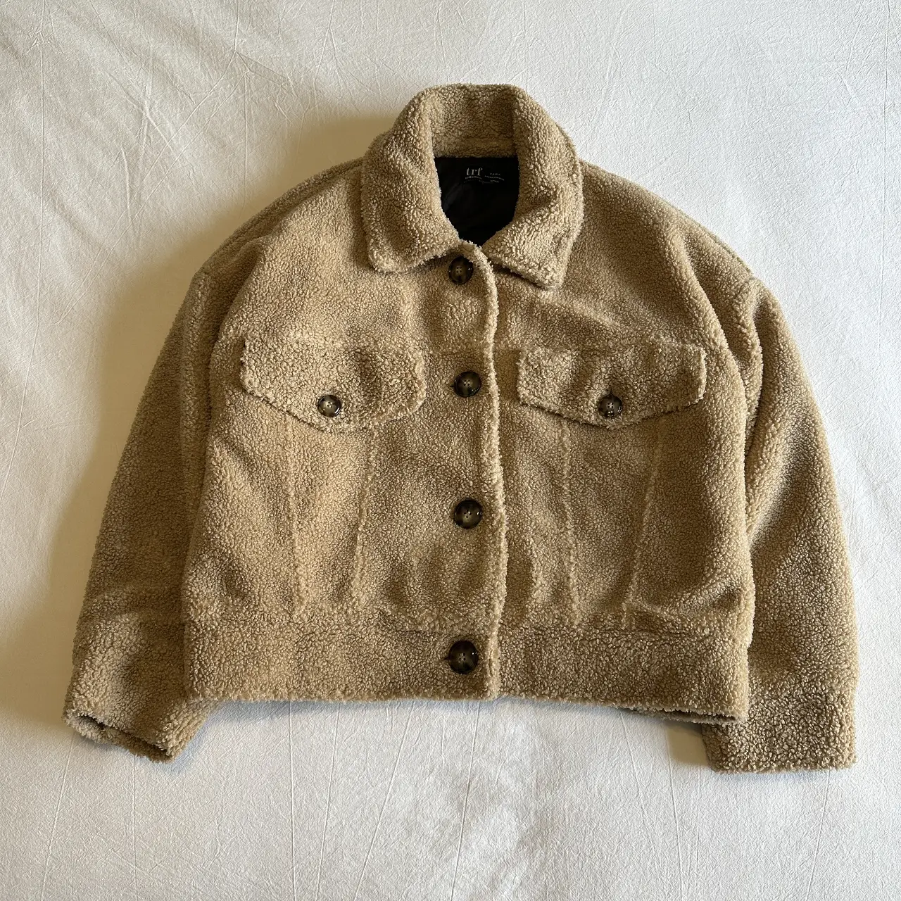 Campera tipo bomber de corderito en color marrón claro. Posee dos bolsillos delanteros y botones para cerrar. En la parte de atrás tiene dos botones para ajustar la cintura. 