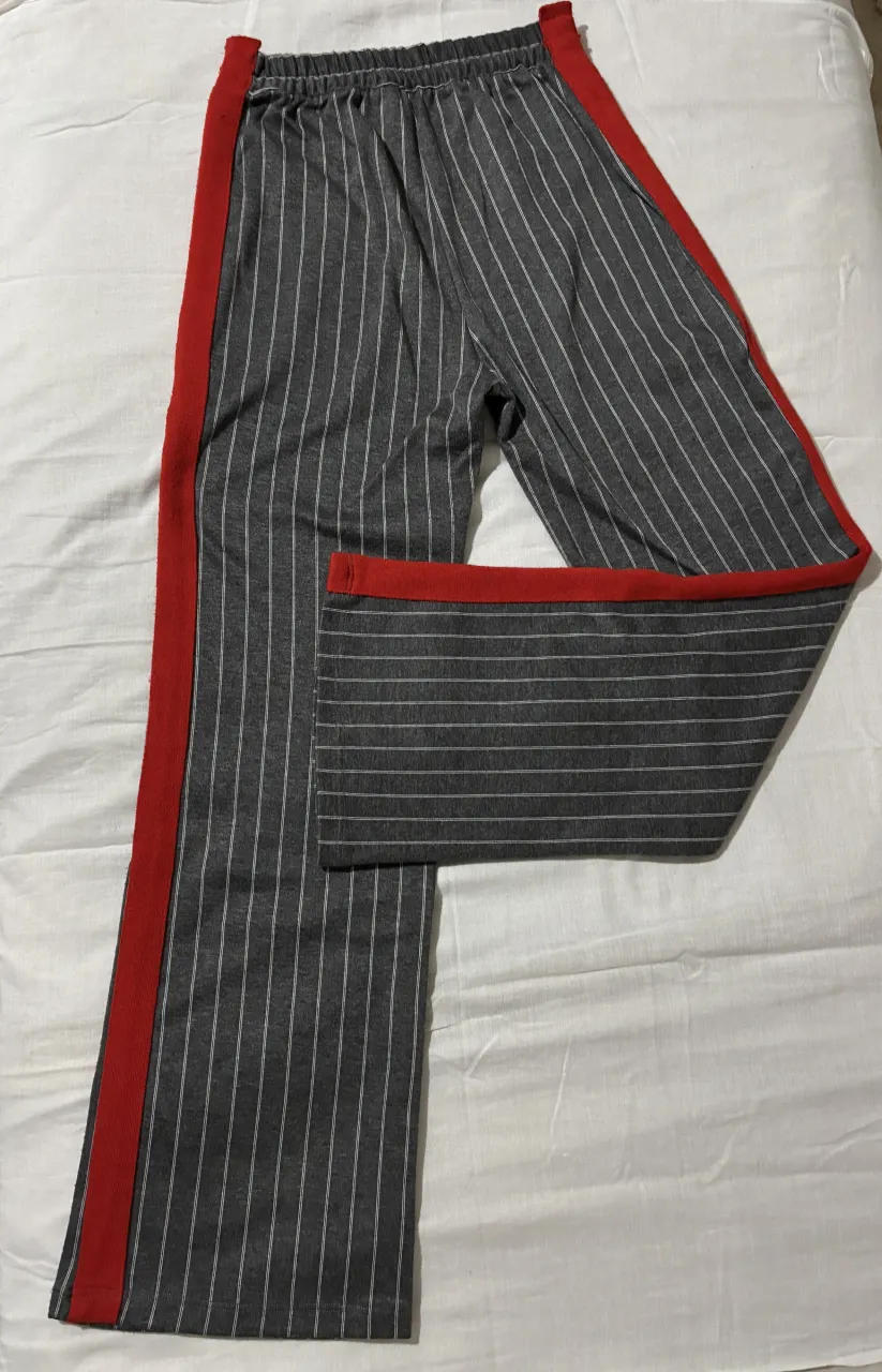 Pantalón de vestir tiro alto a rayas grises con detalles rojos en los laterale. Diseño moderno y cómodo, ideal para un look de noche o formal. 