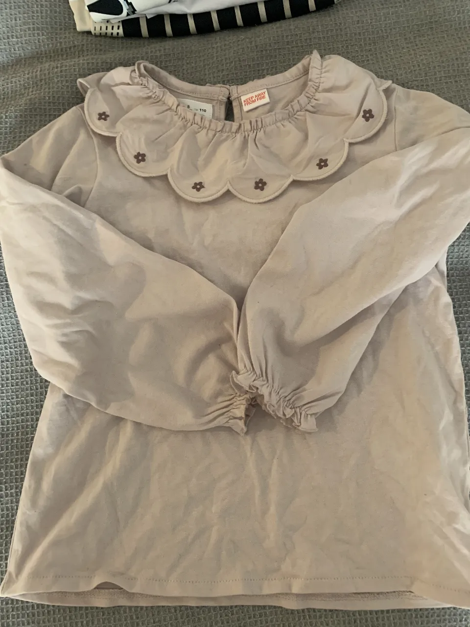 Remera manga larga de algodón color rosa viejo, con cuello redondo y detalles de flores bordadas en el cuello. Puños elastizados.