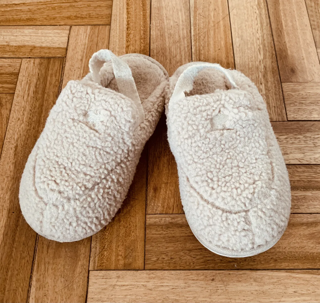 Pantuflas de peluche color crudo con tira de tela.