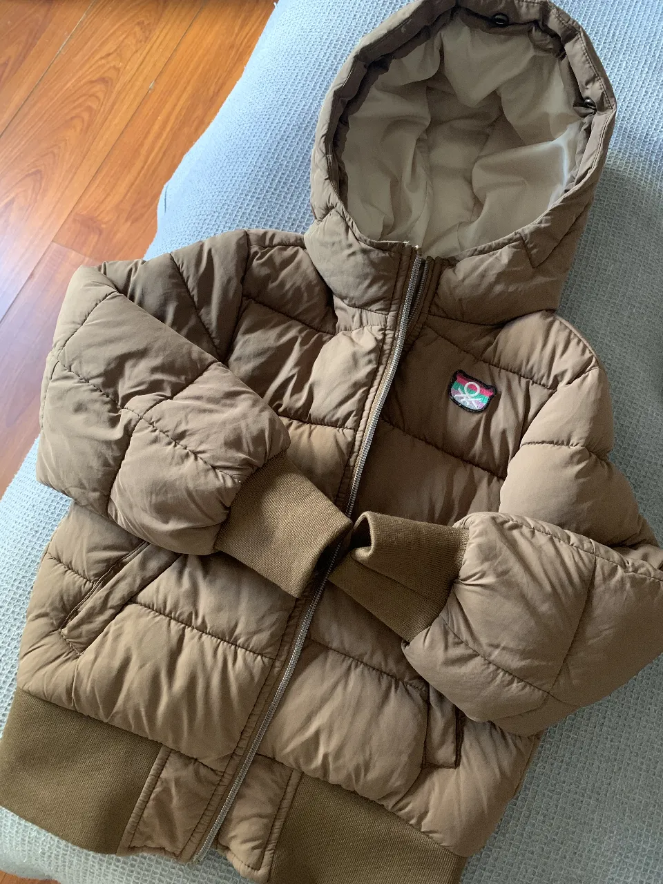 Campera de pluma marrón con capucha, ideal para el invierno. Cuenta con cierre frontal y puños tejidos.