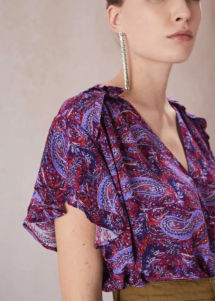 Blusa estampada con diseño paisley en tonos rojos y violetas. Cuello en V y mangas cortas con volados. Ideal para un look casual y con estilo. Impecable y super canchera!