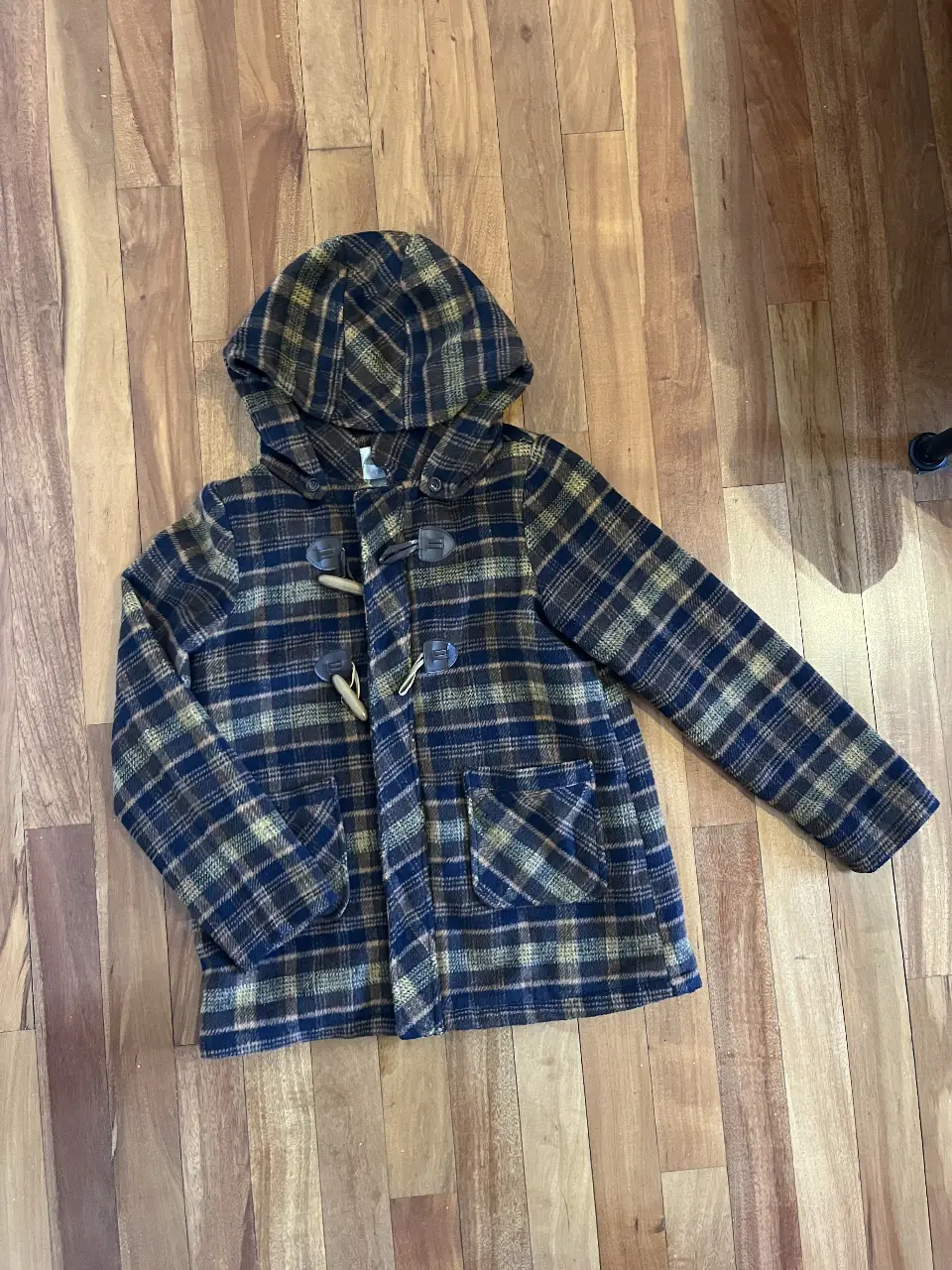 Campera con capucha para niño, de tela escocesa en tonos marrones y azules. Con botones de madera y bolsillos delanteros. Ideal para el invierno.
