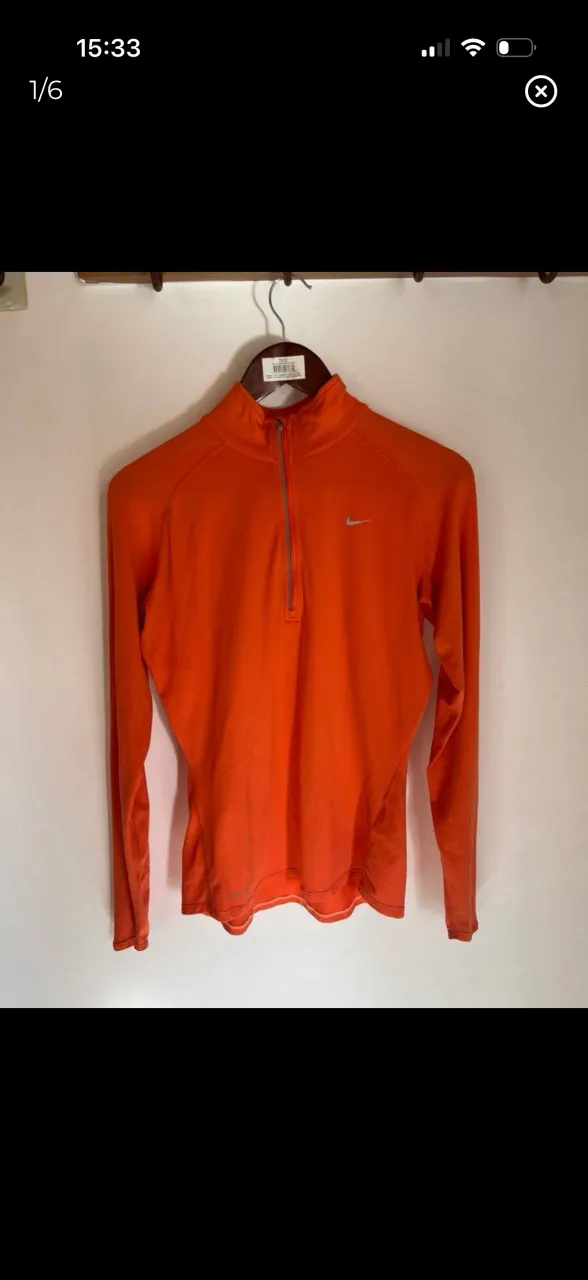 Remera deportiva manga larga naranja con cuello y cierre corto. Logo de la marca plateado en el frente y detalles reflectantes en las mangas.