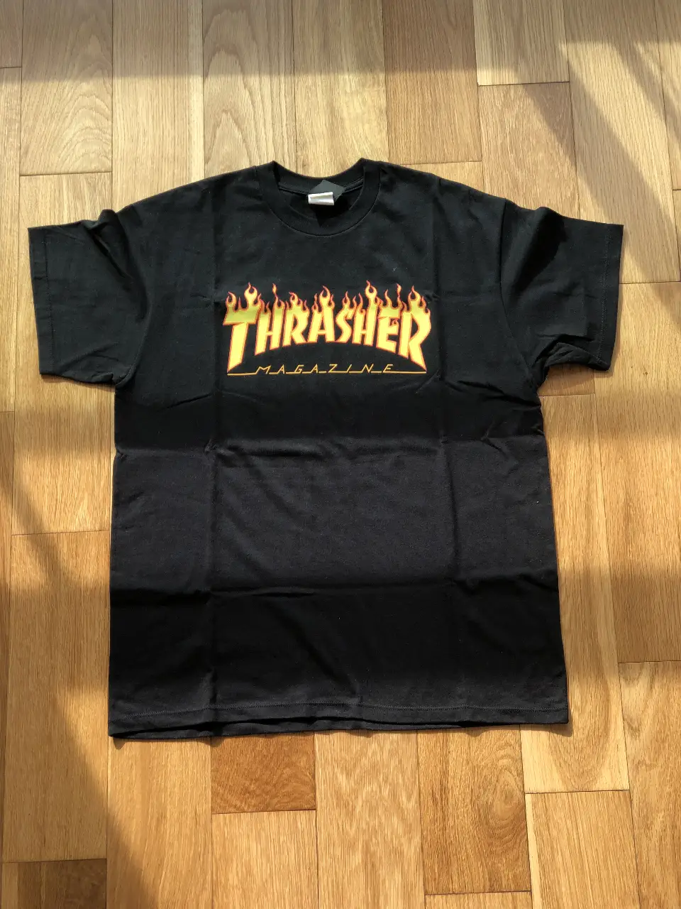 Remera negra de la marca Thrasher con estampado del logo en estilo fuego amarillo y naranja. Talle L.