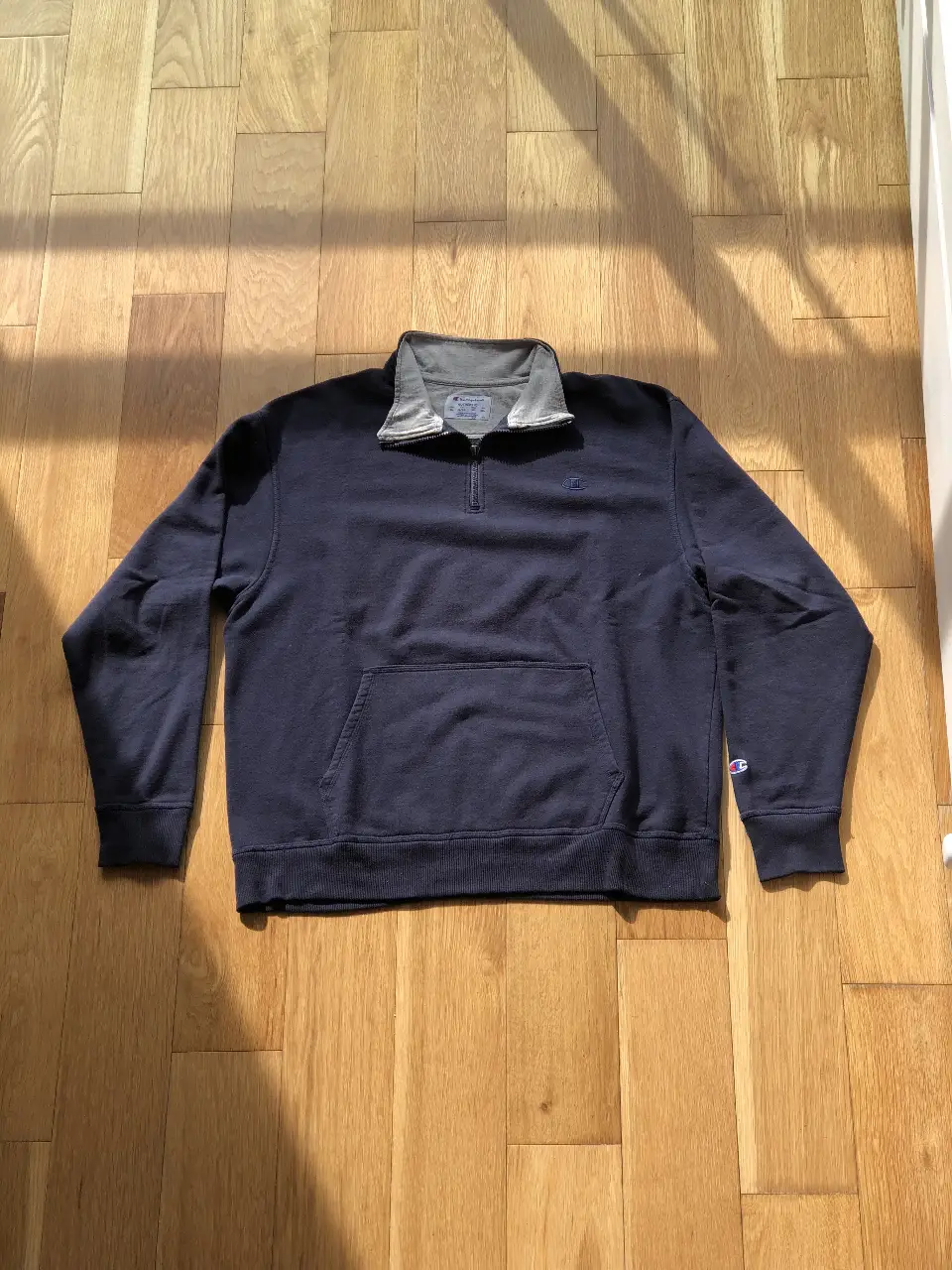 Buzo Champion azul marino con cierre y cuello alto gris. Logo bordado en el pecho. Talle XL.