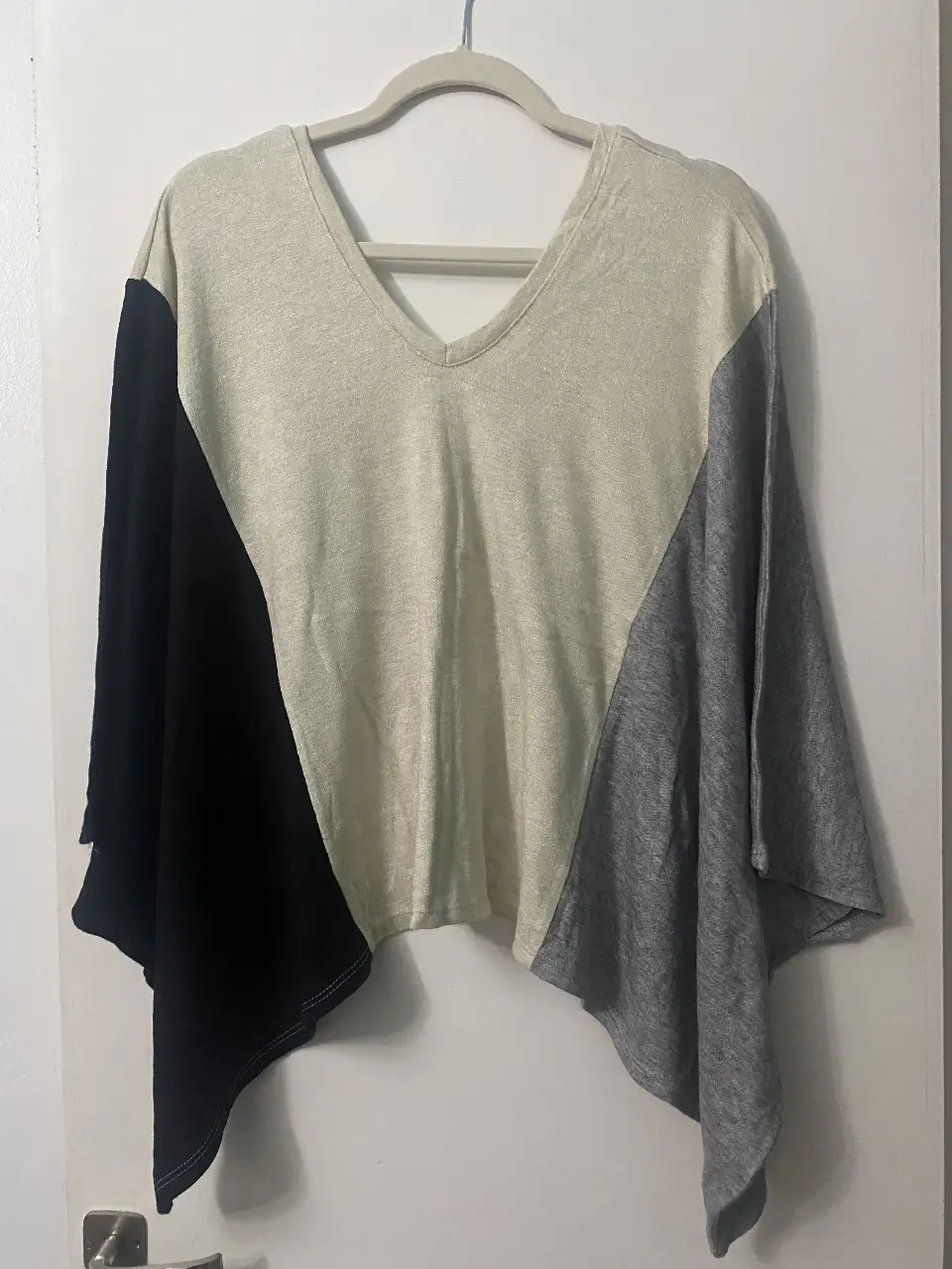 Sweter tipo poncho con cuello en V, combinada en negro, gris y crudo. Ideal para un look casual y canchero.