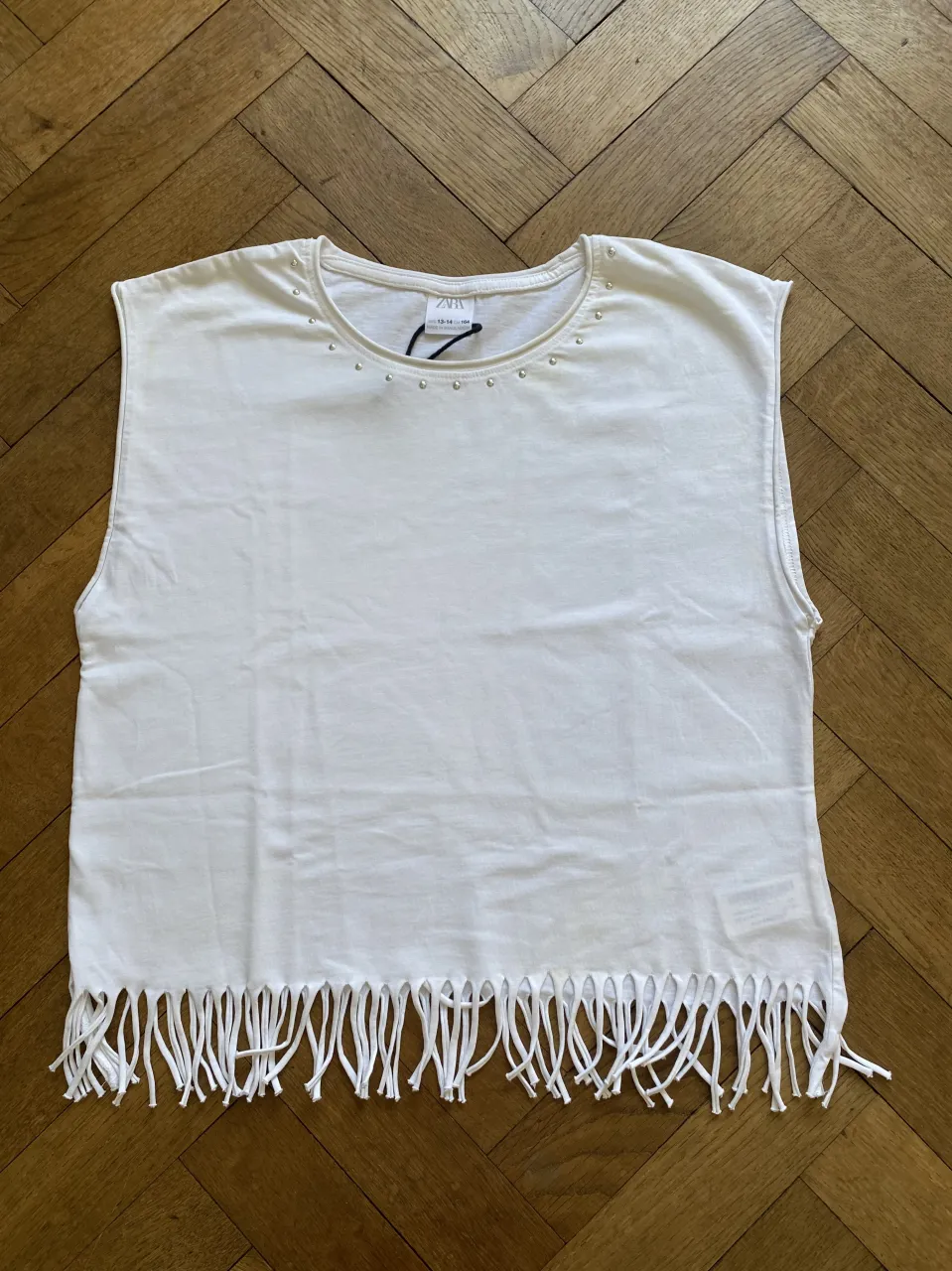 Musculosa blanca con tachitas plateadas en el cuello y flecos en el ruedo. ¡Un toque canchero y original para cualquier look! en la parte trasera arriba a la izquierda  tiene una pequeña  mancha amarilla y en la parte delantera tiene alguna otra,  ( en la foto se aprecia bien el tipo de mancha ) 