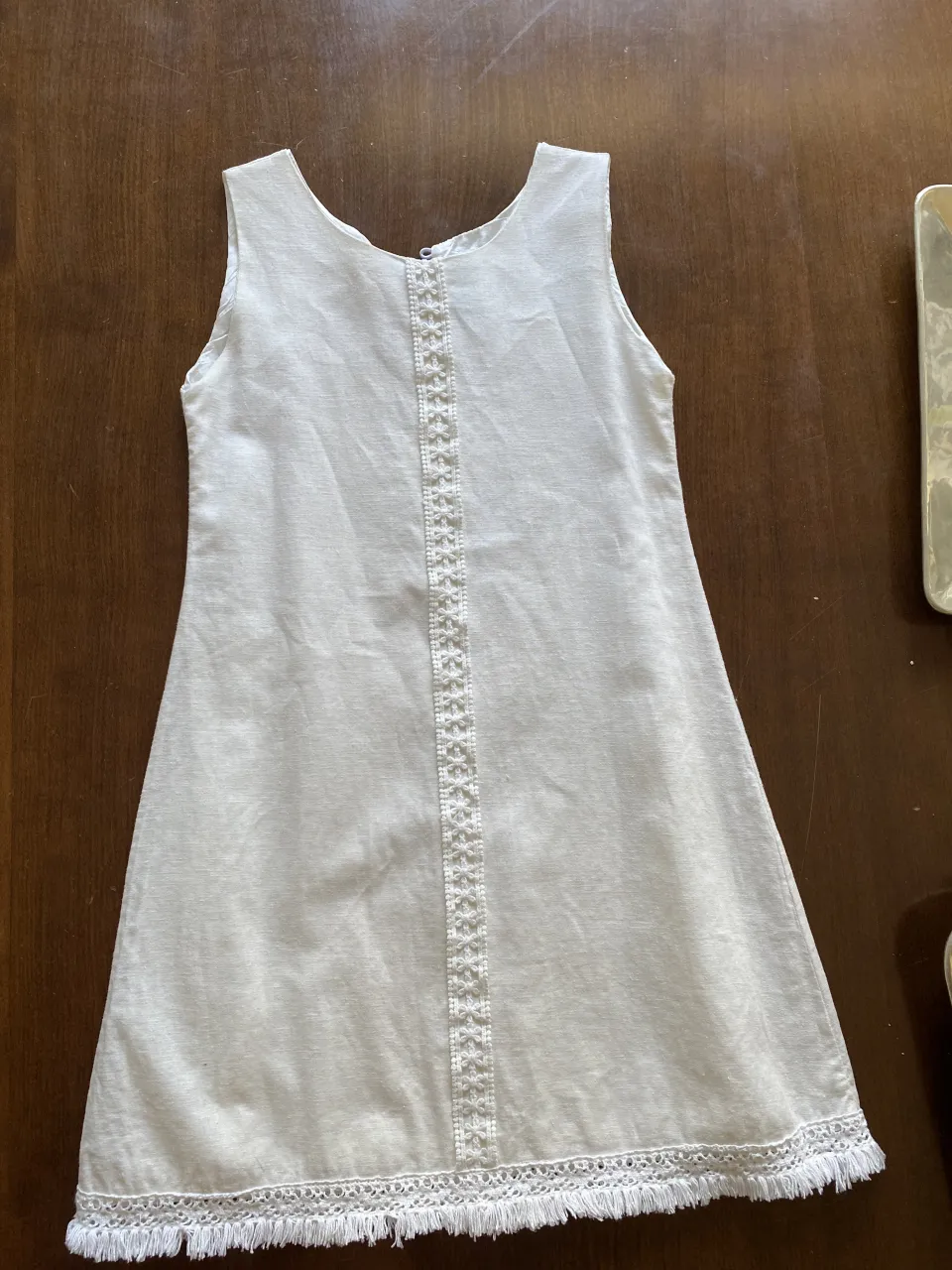 Vestido blanco de lino con detalles de puntilla y flecos en el ruedo. Ideal para un look fresco y delicado.
