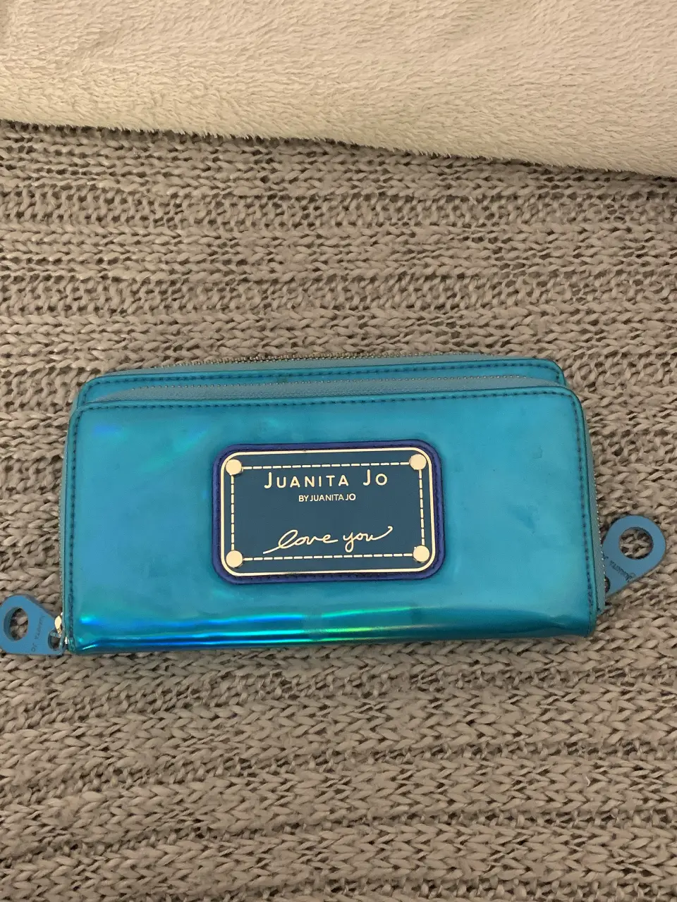 Billetera de mujer Juanita Jo, color azul tornasolado, con cierre y detalles en azul oscuro. Diseño con la frase 'Love you'. Ideal para llevar tus esenciales con estilo.