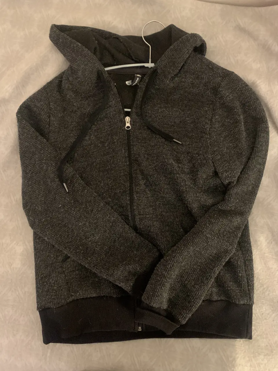 Buzo con cierre gris oscuro, con capucha y bolsillos. Ideal para el invierno, cómodo y abrigado. Perfecto para un look casual.