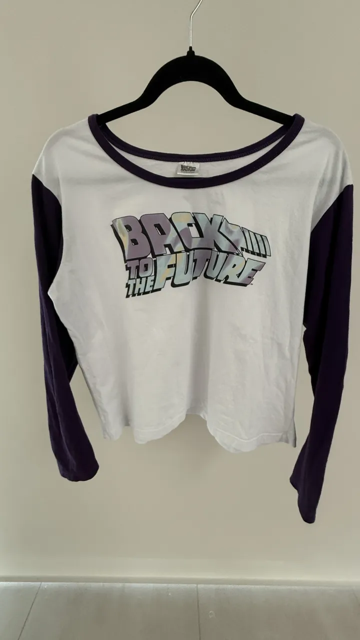 Remera manga larga blanca con mangas y cuello de color morado. Estampa frontal de "Back to the Future". medidas, hombros 46, sisa 53, largo total 50, mangas 55