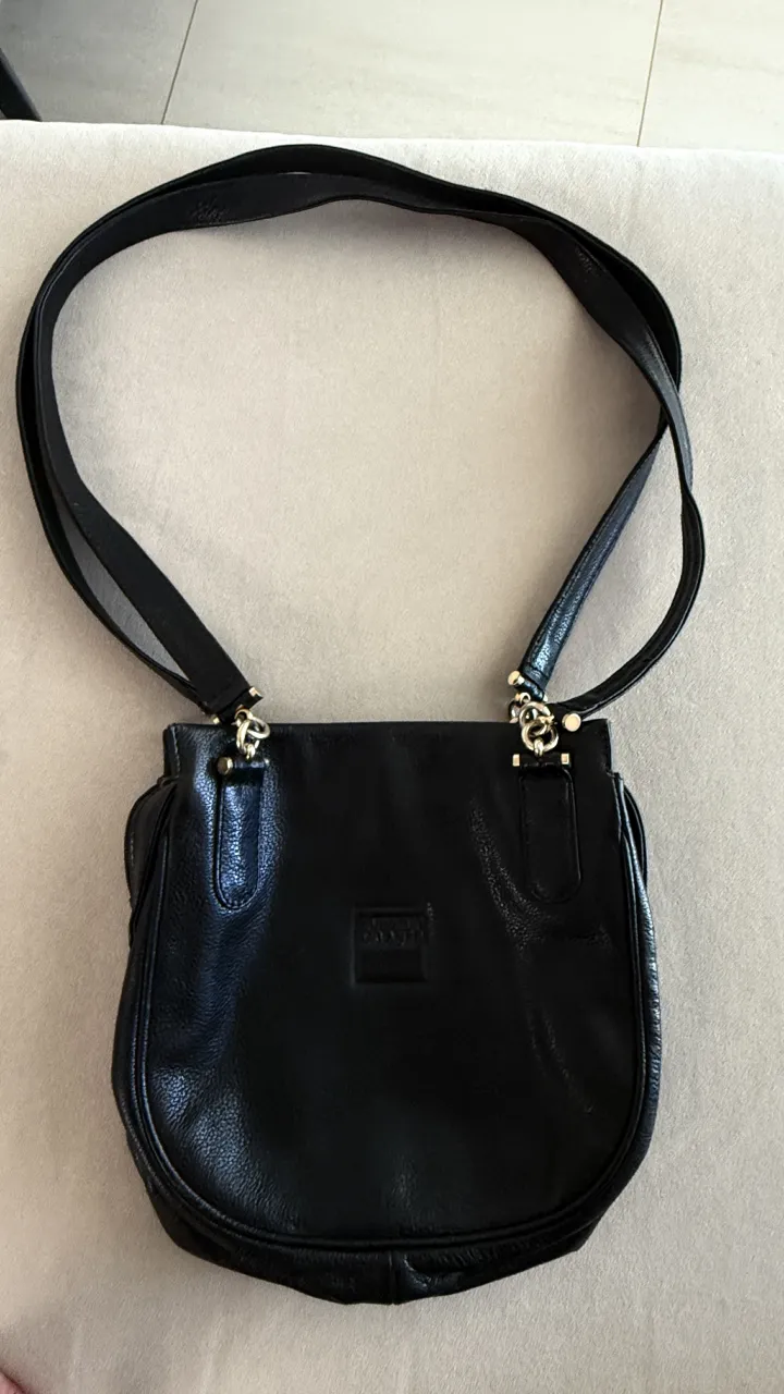 Cartera negra de cuero . Posee múltiples compartimentos internos, 
Medidas: alto 25, ancho 25, fuelle 12, largo correa 43