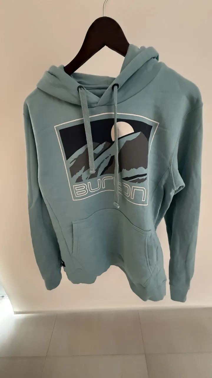 Buzo con capucha marca BURTON , estampa de montañas y sol. Ideal para un look casual y urbano. Posee bolsillo canguro al frente y cordones regulables en la capucha.

Medidas en la ultima foto
