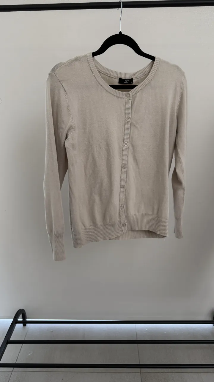 Cardigan de tejido fino, color crudo, con botones al frente y cuello redondo. Mangas largas y puños elastizados. talle unico, va hasta un M. medidas en fotos