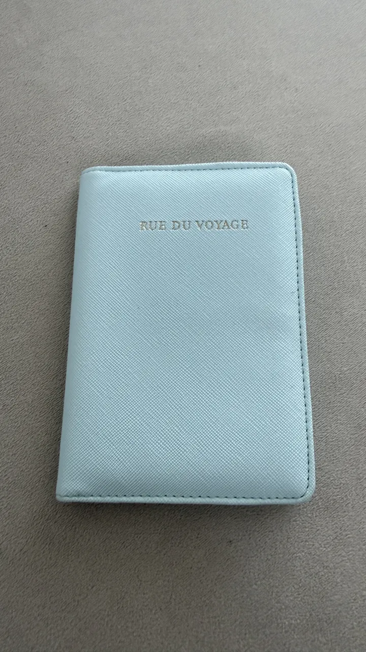 Porta pasaporte celeste con inscripción "RUE DU VOYAGE" en dorado. Posee compartimentos internos para tarjetas y cierre a presión.
Medidas: alto 14 , ancho 10