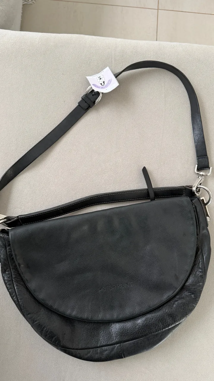 Cartera negra de cuero con textura y correa ajustable. Posee un bolsillo exterior con cierre y el interior está forrado con tela estampada con el logo de la marca.
Marca Peter kent. detalles: presenta desgate de uso en correa y detalles en herrajes metalicos