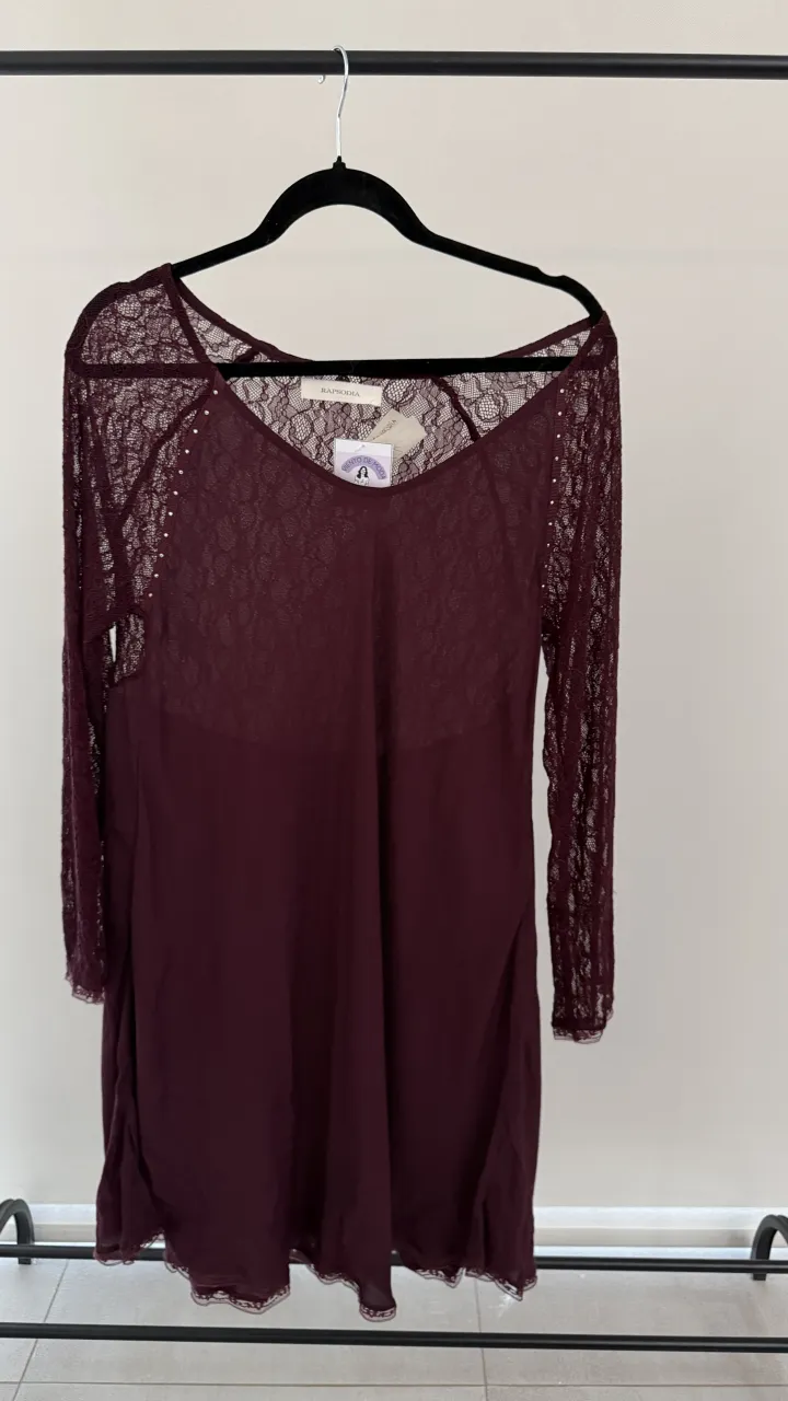 Vestido de manga larga de encaje color bordó con detalles de pequeñas tachas plateadas en el escote. Posee un forro interior de tela lisa. Medidas en la publicación 