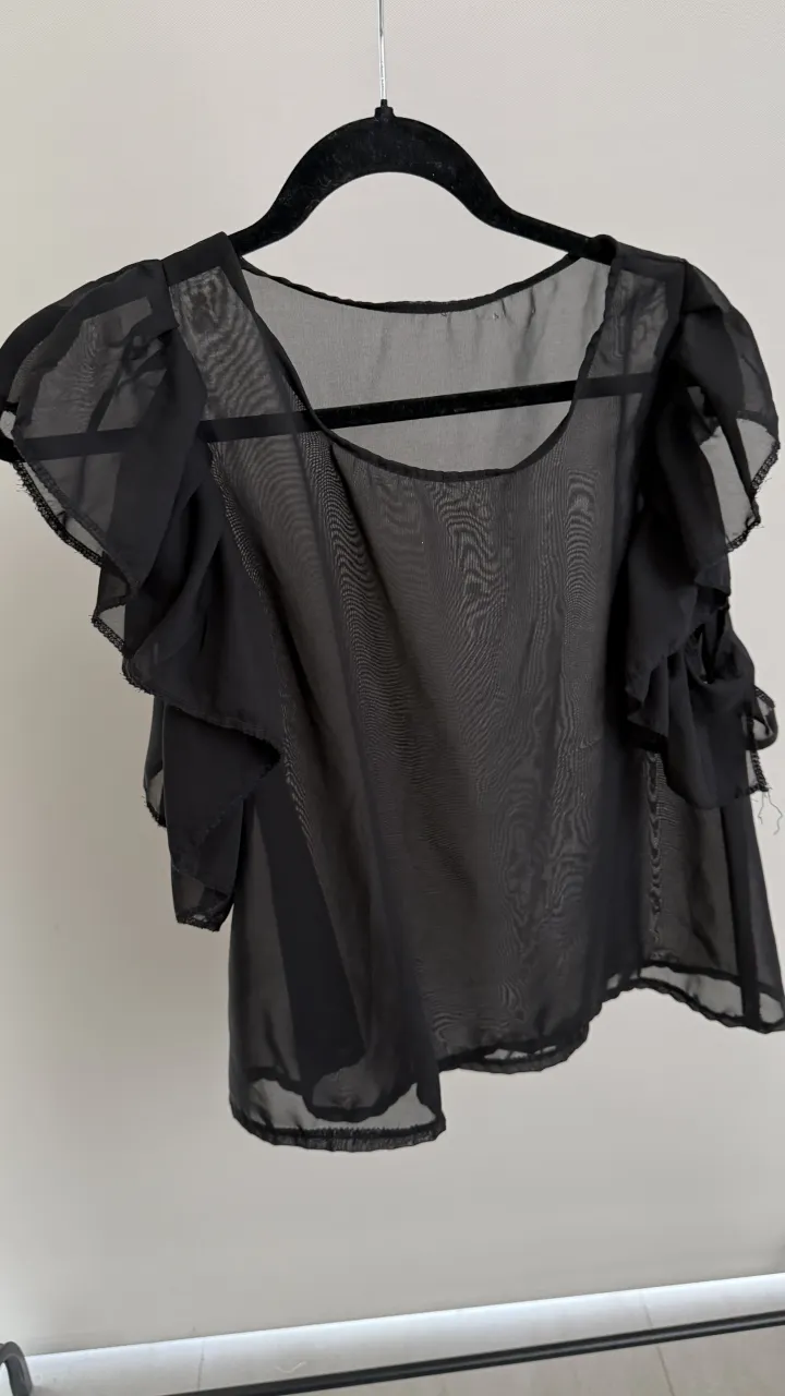 Blusa negra con mangas cortas abullonadas y volados. Escote redondo. va para un xs