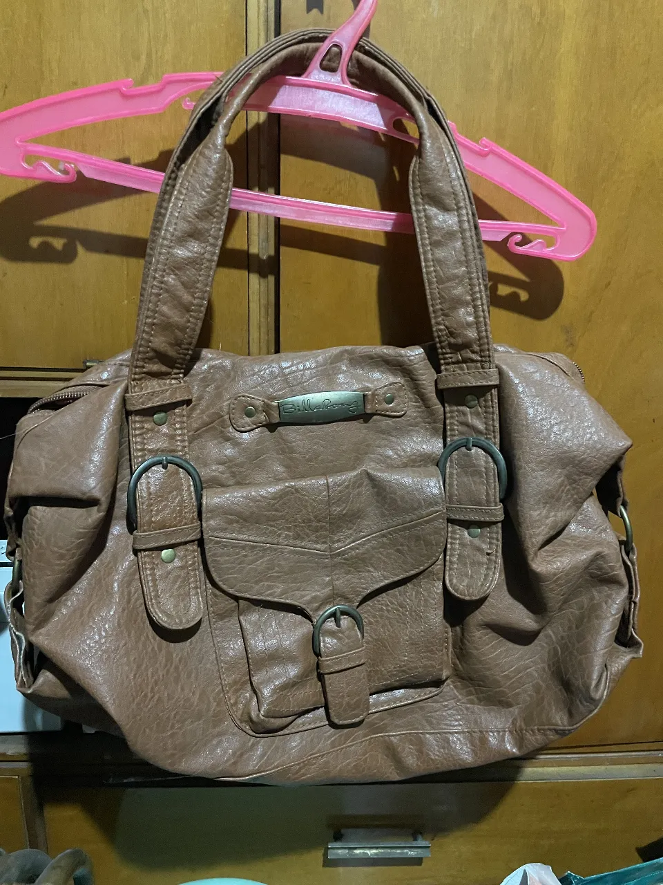 Bolso marrón de cuero sintético con detalles de hebillas y bolsillo frontal. Ideal para llevar todo lo necesario con estilo.