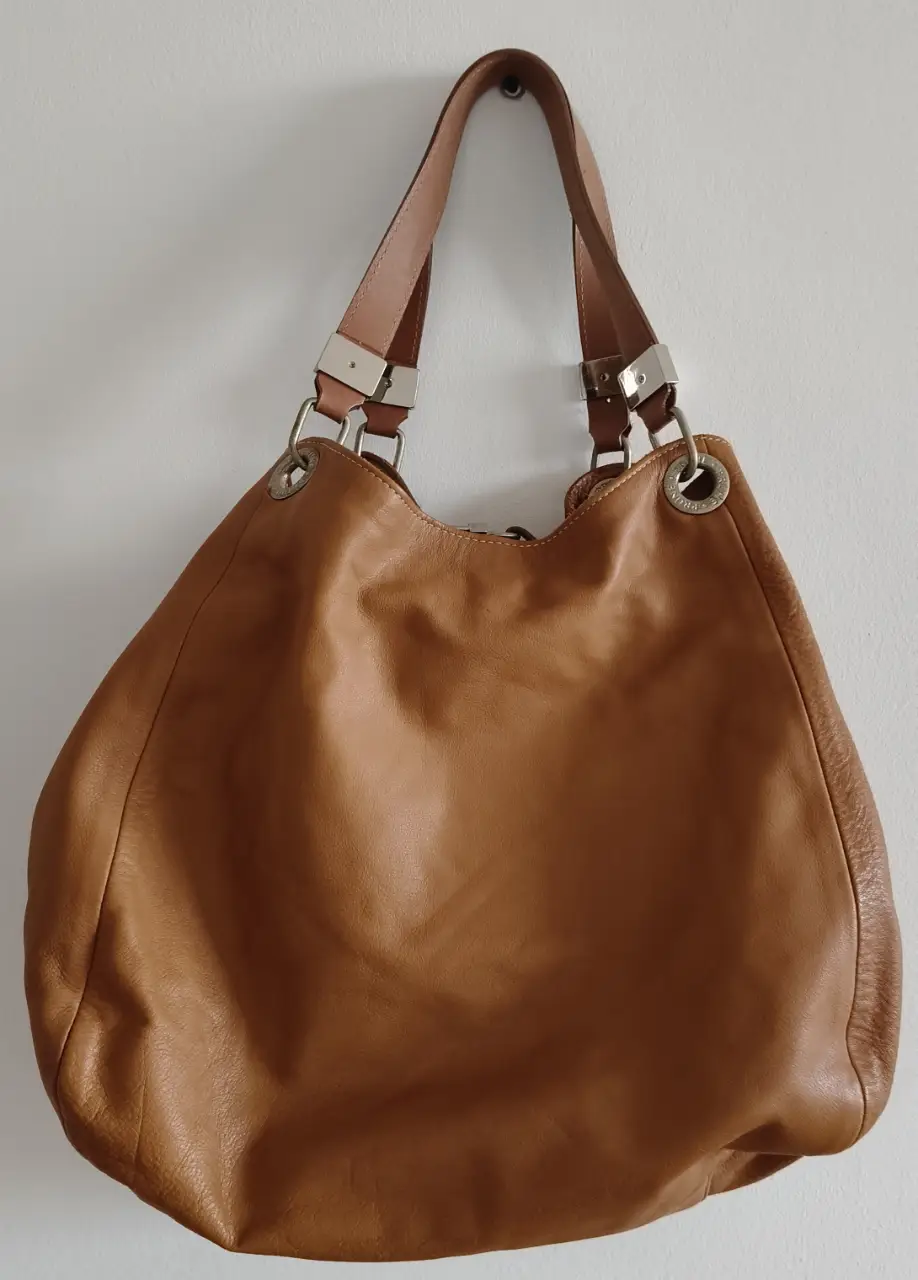 Cartera de hombro de cuero marrón de la marca Prune. Diseño amplio y cómodo, ideal para llevar todo lo necesario. Detalles metálicos plateados y forro interior con logo de la marca. Perfecta para un look casual y elegante.