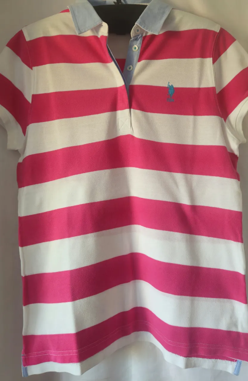 Remera polo de mujer a rayas horizontales en rosa y blanco. Cuello y detalles en celeste. Logo de la marca bordado en celeste. Talle XL.