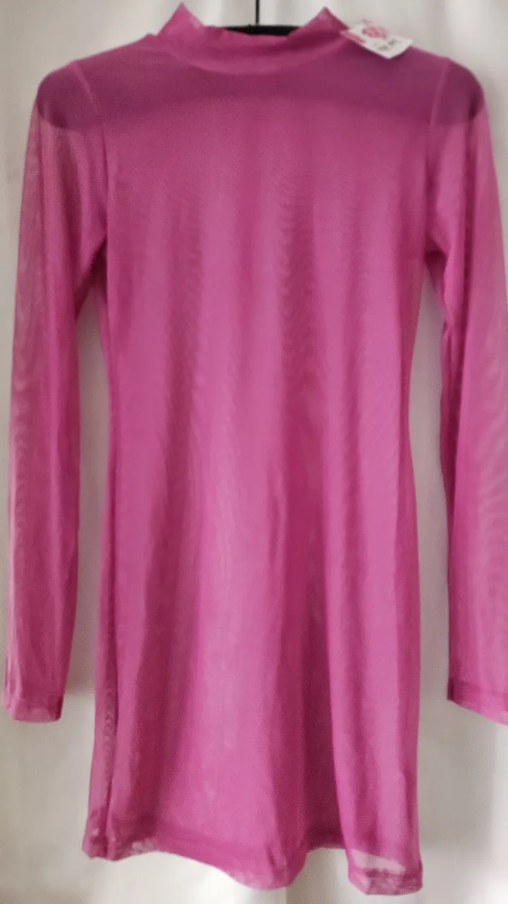 Vestido mini de red transparente en color rosa chicle, con cuello alto y mangas largas. Ideal para usar sobre otra prenda o como un toque audaz.