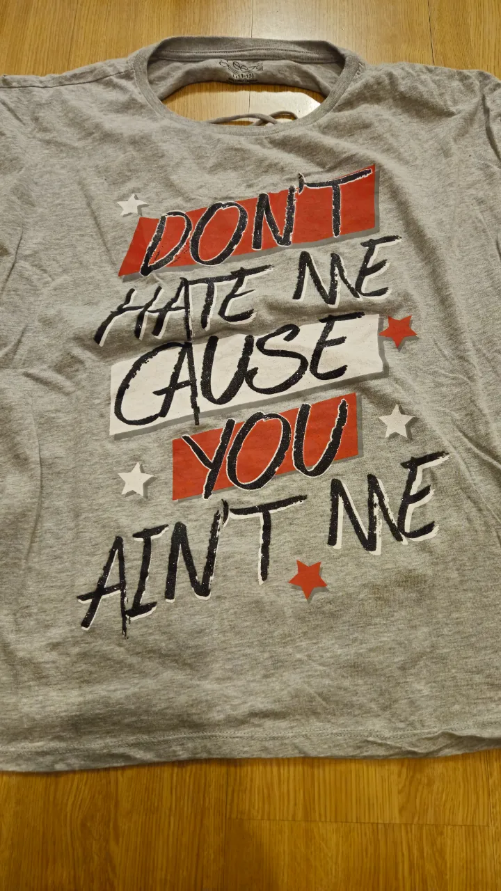 Remera de hombre gris con estampado "Don't hate me cause you ain't me" en rojo y negro. Diseño con espalda calada.