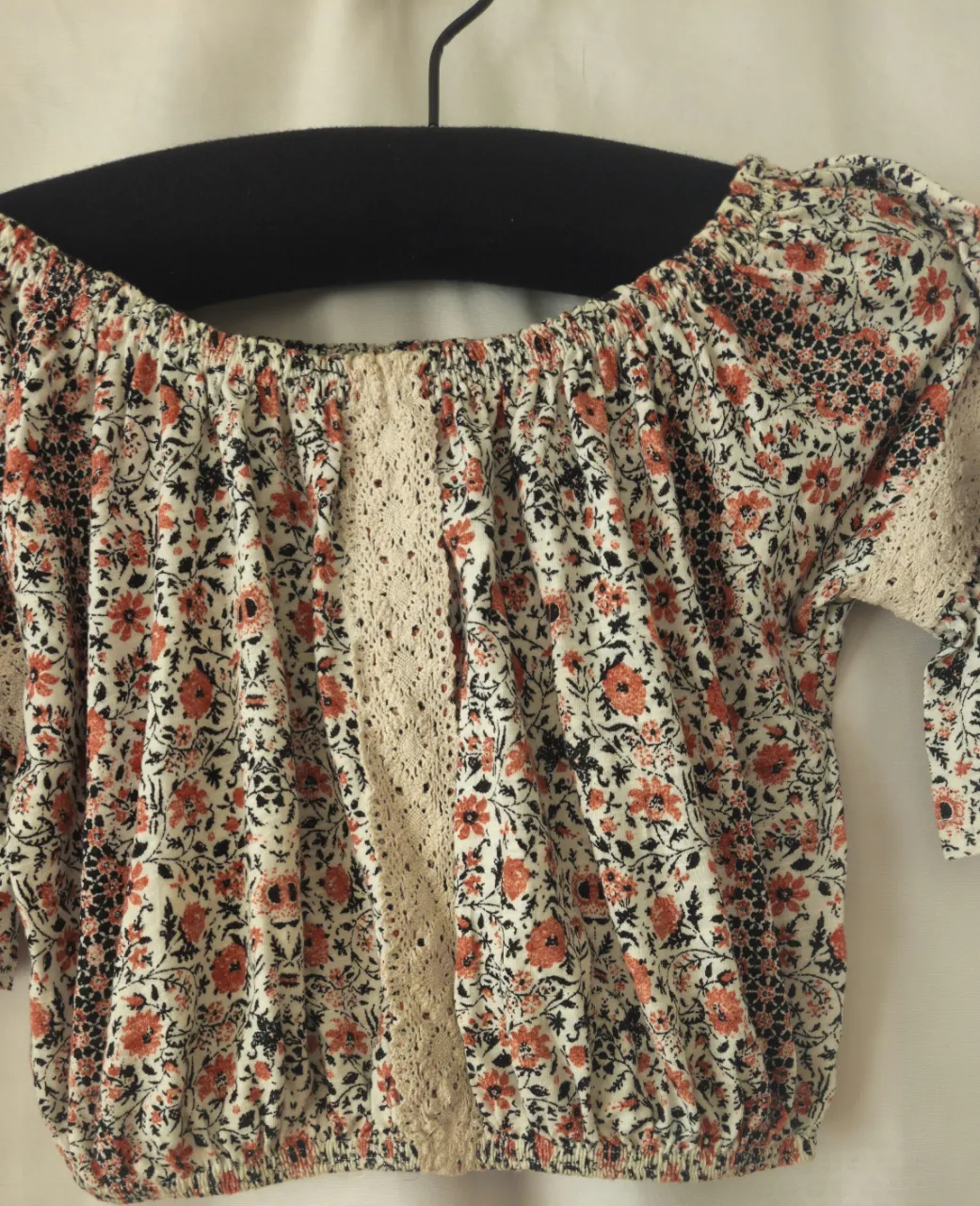 Blusa de mujer con estampado floral en tonos naranja, blanco y negro. Diseño off-shoulder con detalles de encaje y mangas 3/4. Ideal para un look bohemio y fresco.