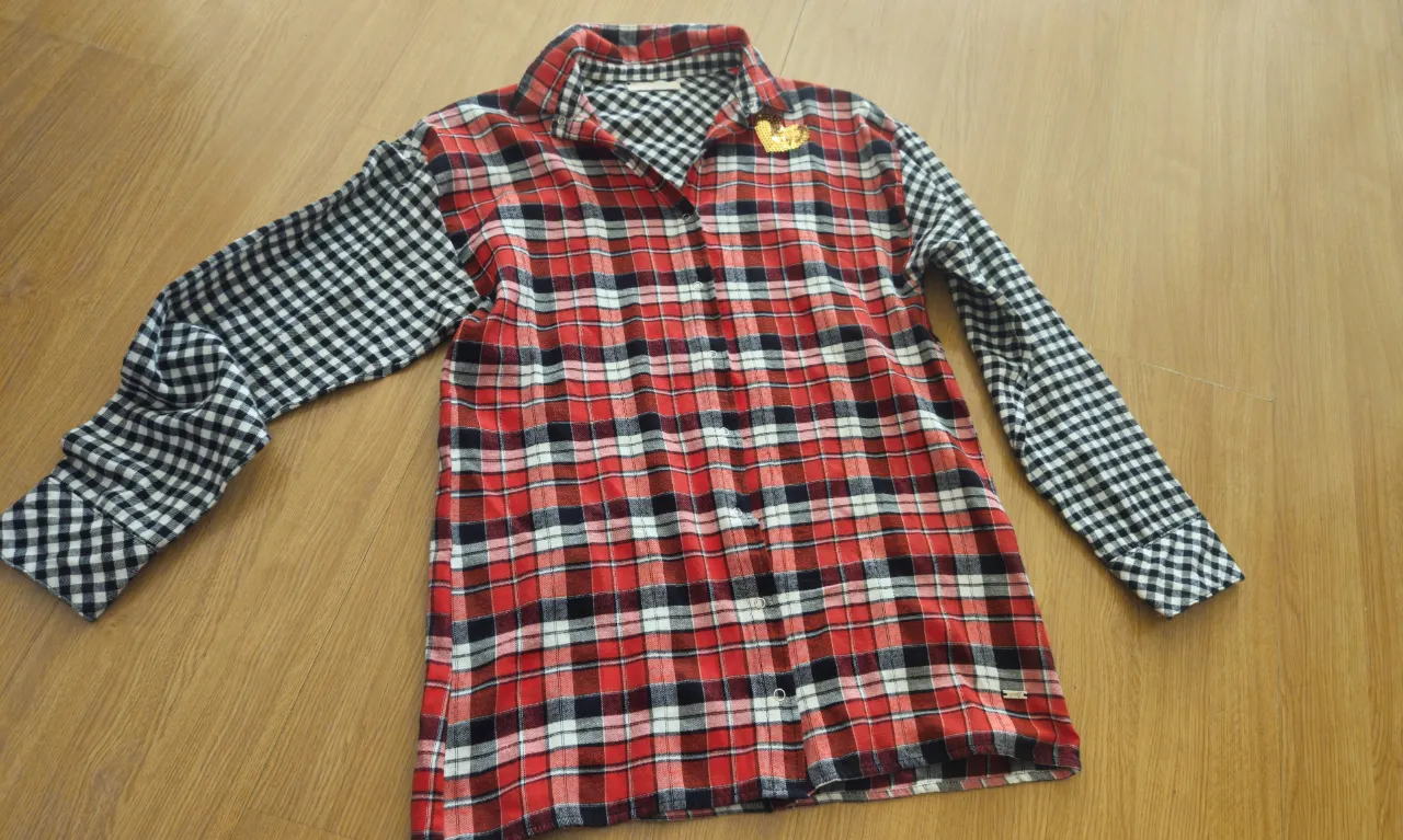 Camisa a cuadros roja y negra con mangas en contraste de cuadros blanco y negro. Detalle de aplique dorado con forma de corona en el pecho y número 21 con lentejuelas en la espalda. Ideal para un look casual y con onda.