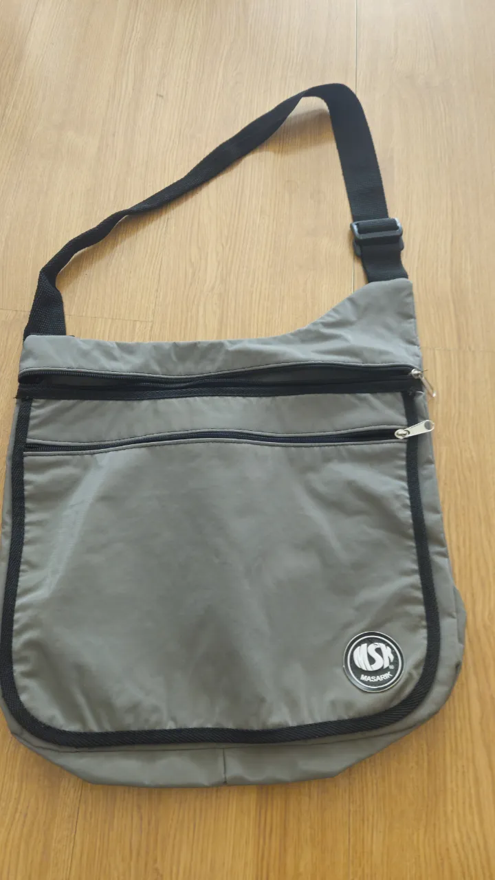 Bandolera gris con detalles en negro, ideal para llevar tus esenciales con estilo y comodidad. Perfecta para el día a día. Medida 38*31 cm.