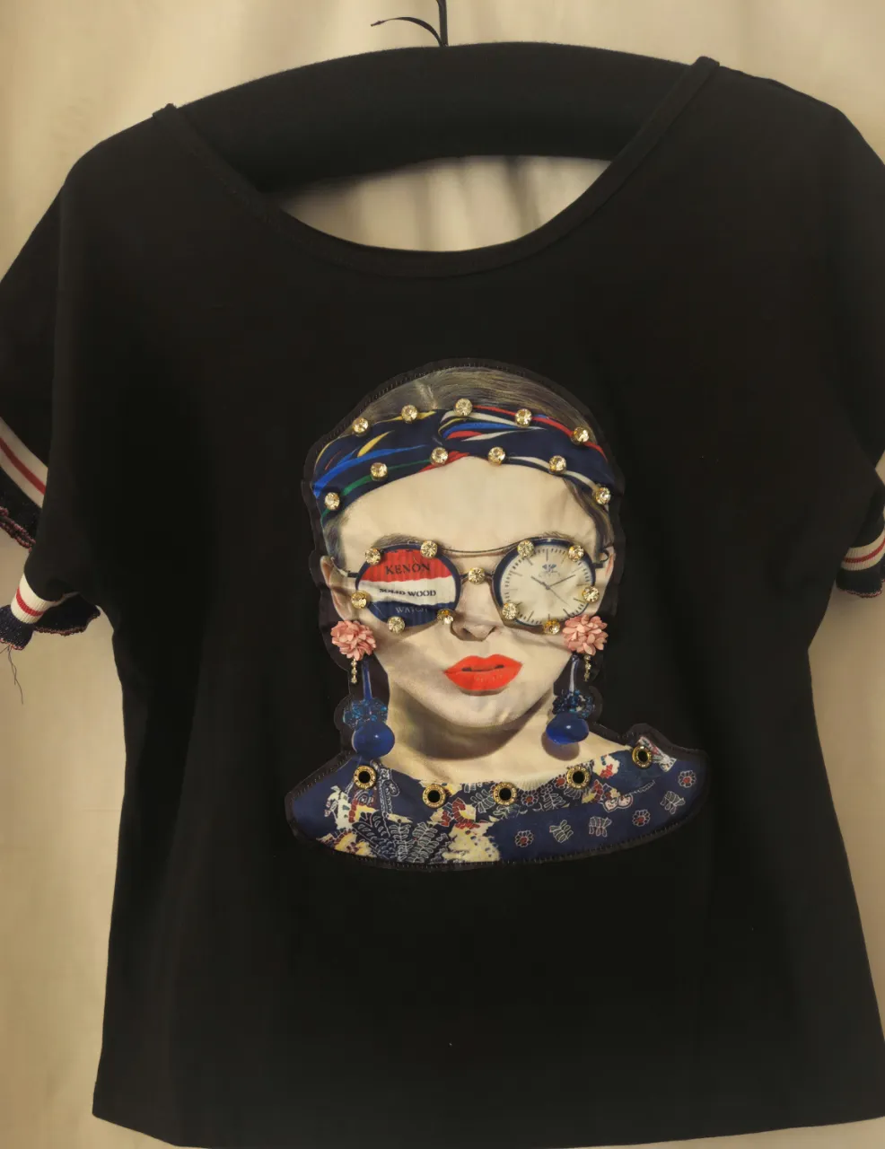 Remera negra con estampado de rostro femenino con gafas y detalles de pedrería. Diseño original y llamativo, ideal para un look moderno y con estilo.