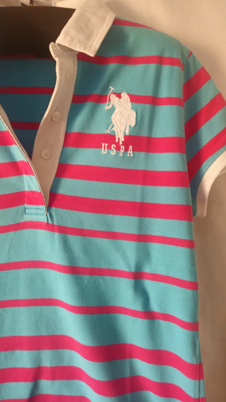 Remera polo de mujer, a rayas horizontales en color turquesa y rosa. Cuello y mangas blancas. Con logo de la marca US Polo Assn.