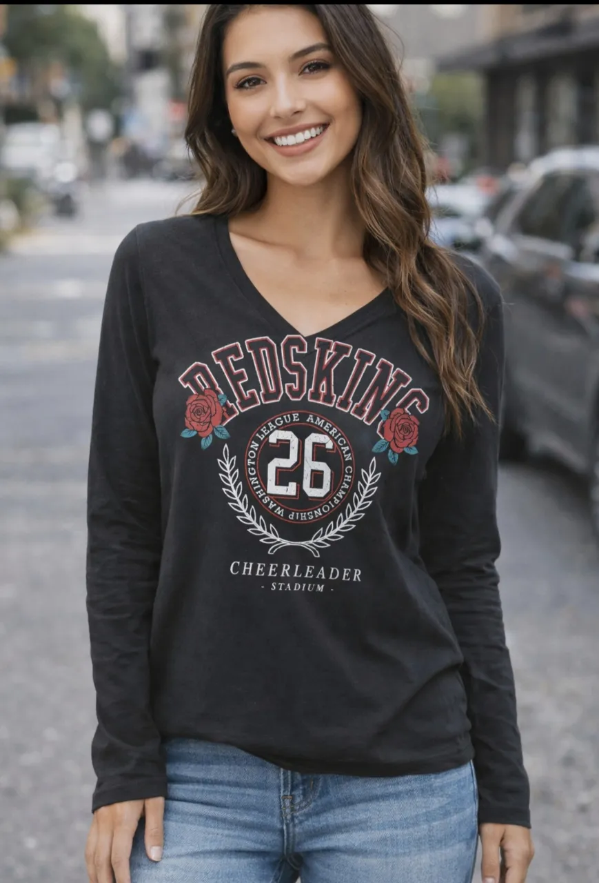 Remera de manga larga con cuello en V y estampa "REDSKINS" con dos rosas y el número "26" en el frente. La estampa incluye "WASHINGTON LEAGUE AMERICAN CHAMPIONSHIP" y "CHEERLEADER STADIUM".