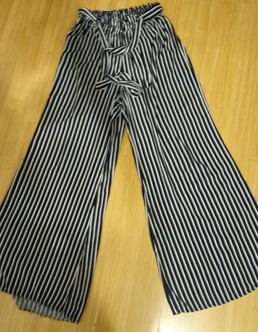 Pantalón palazzo a rayas verticales en blanco y negro, con cintura elastizada y lazo para ajustar. Ideal para un look fresco y moderno.