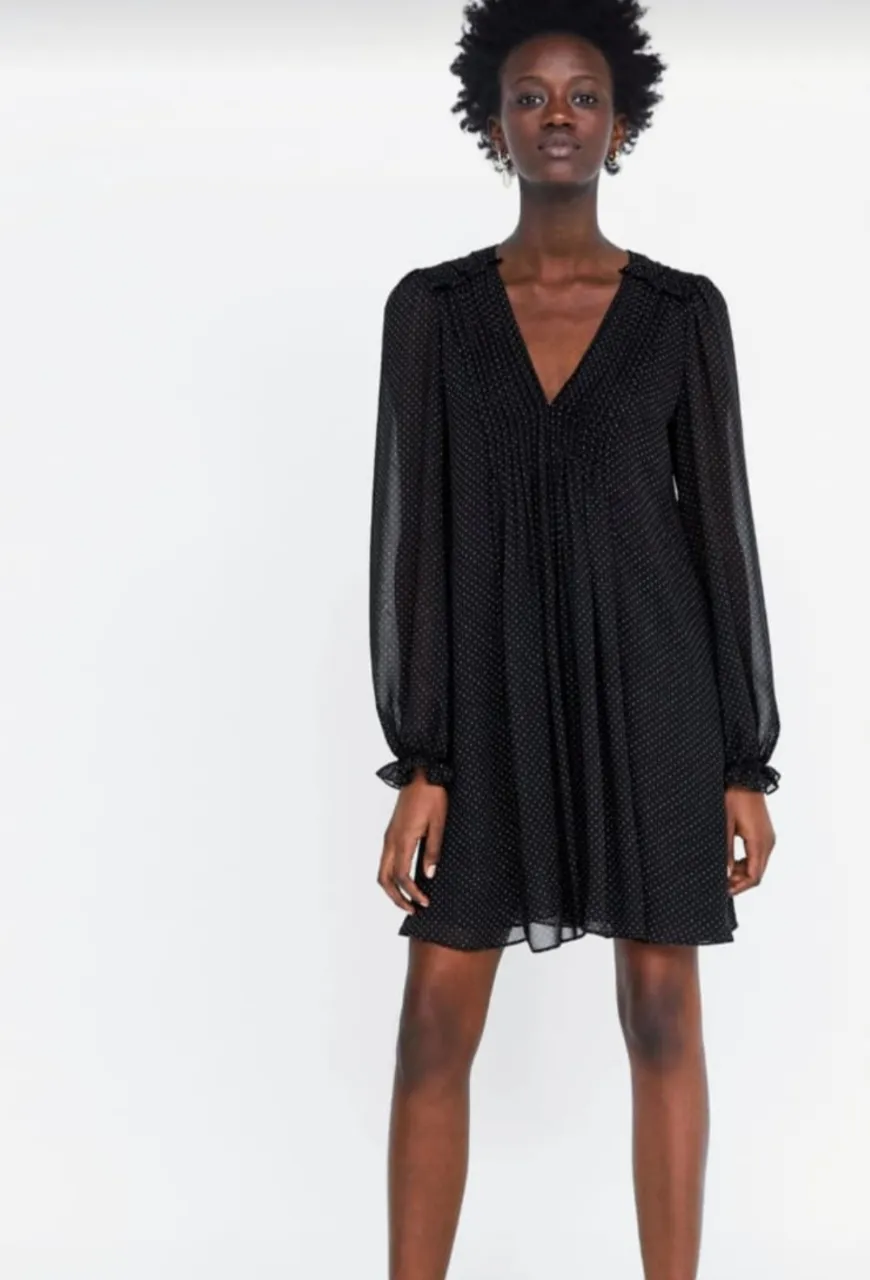 Vestido mini negro con estampado de lunares. Diseño con cuello en V y mangas largas con puños. Ideal para una salida o evento especial.