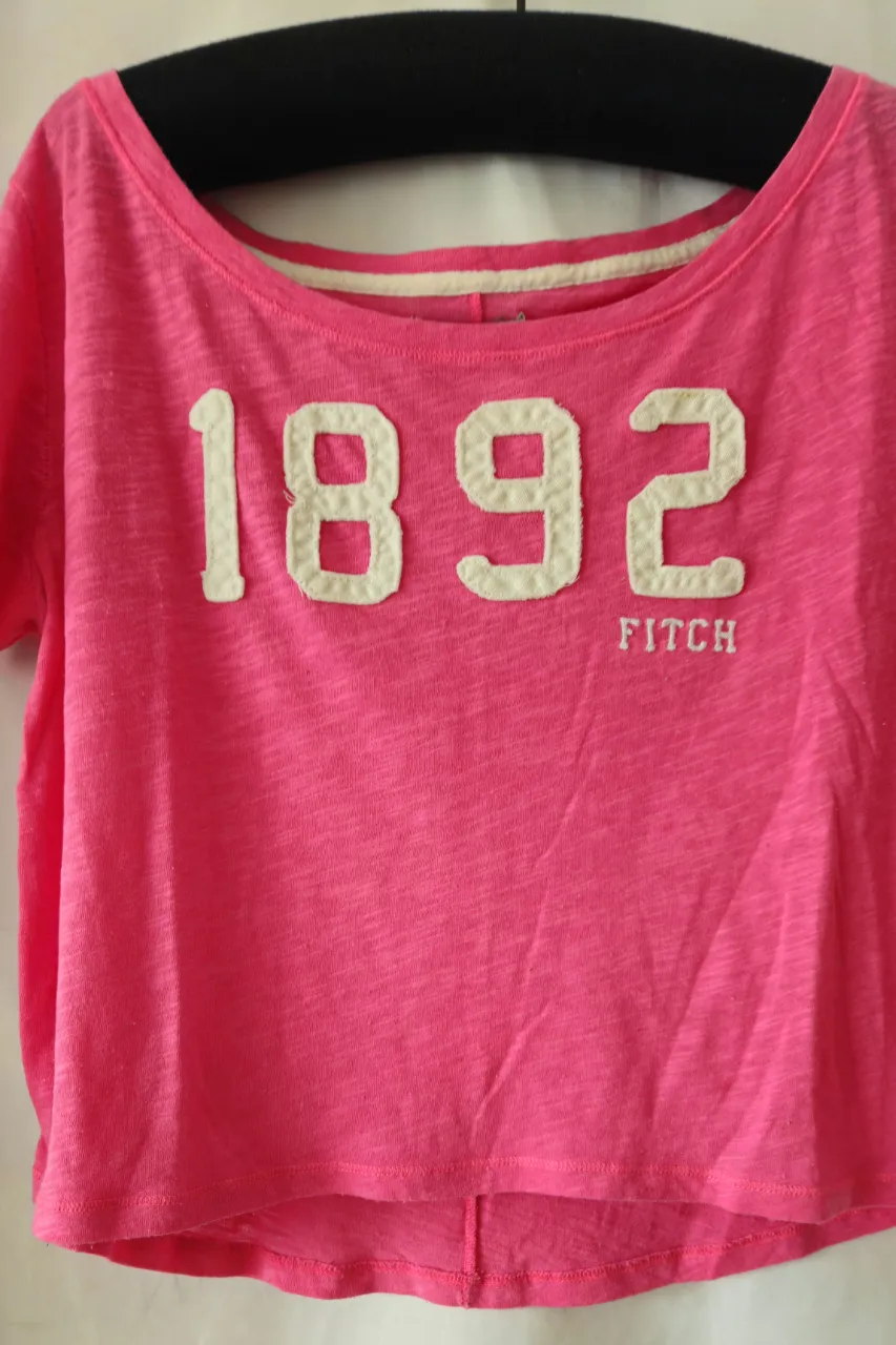 Remera rosa de manga corta de la marca Abercrombie & Fitch, con el número 1892 en blanco en el frente. Ideal para un look casual y cómodo.